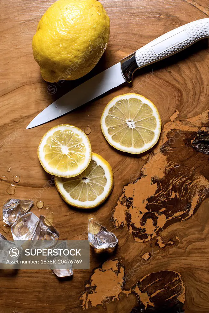 Whole Lemon and Lemon Slices with Knife and Ice Cubes on Wood Table