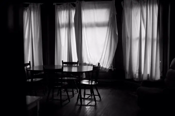 Dark Room With Drapes Covering Windows Behind Table and Chairs