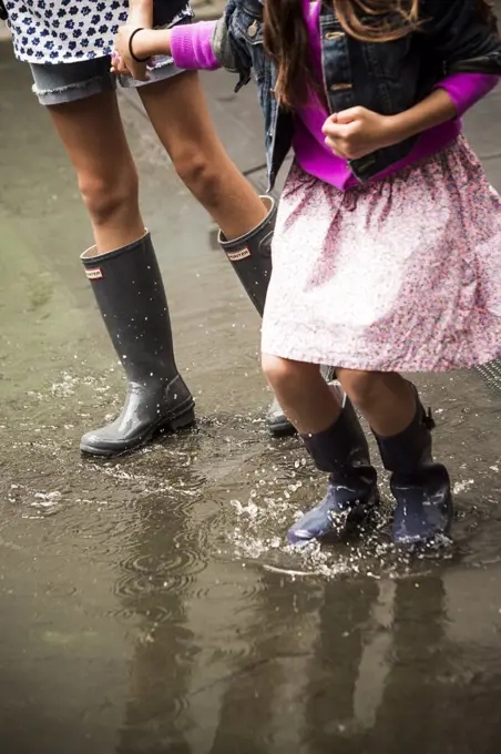 Two Young Girls Walking Through Puddle in Rubber Boots