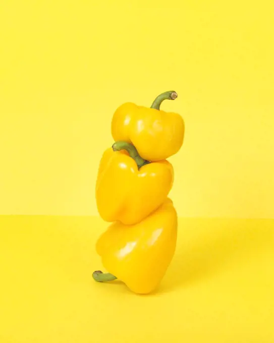 Three Stacked Yellow Peppers against Yellow Background