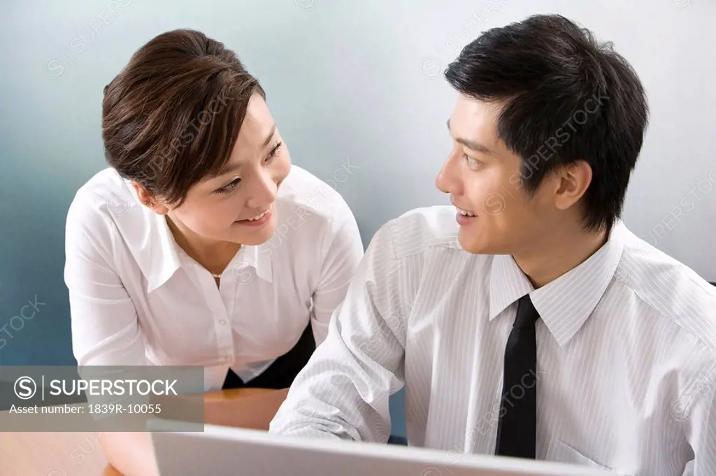 Young businessman and businesswoman using laptop in office