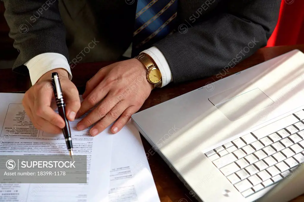 Man Sitting Next To Computer Writing On A Document