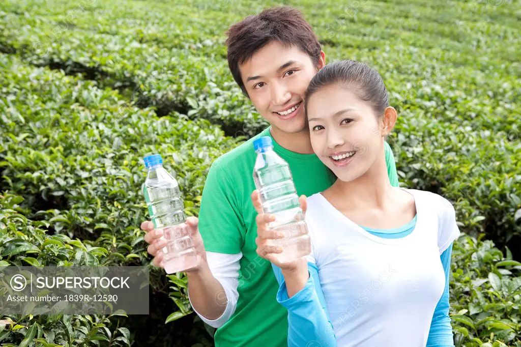 Young Couple in a Tea Field Holding Water Bottles
