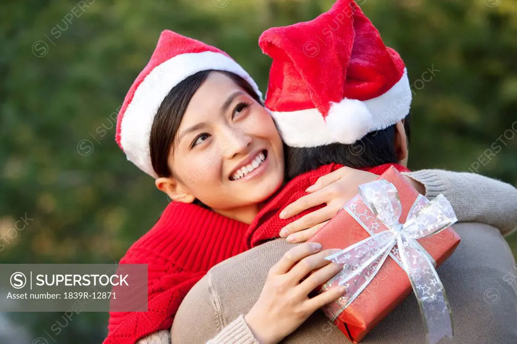 Young Woman Embraces Young Man while Holding Christmas Gift