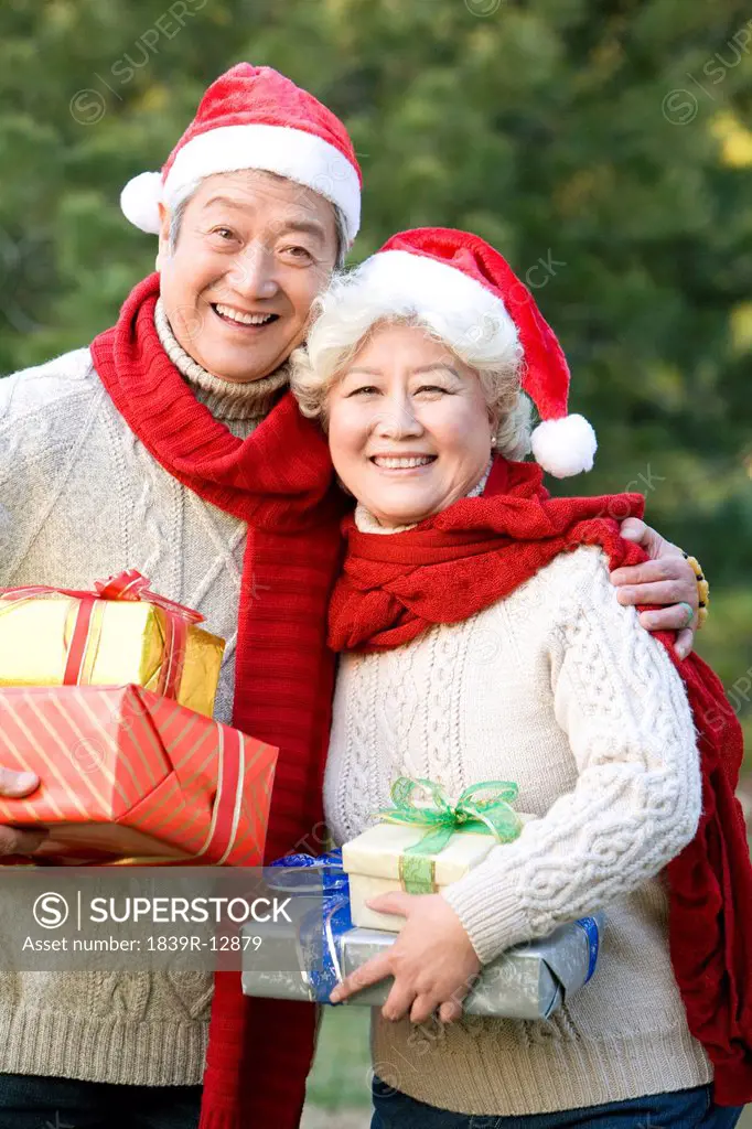 Senior Couple in Santa Hats Holding Christmas Gifts