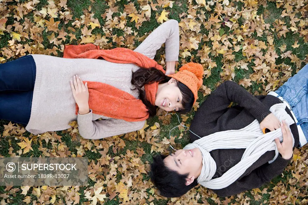 Young Couple Lying Amonst Maple Leaves Listening to MP3 Player