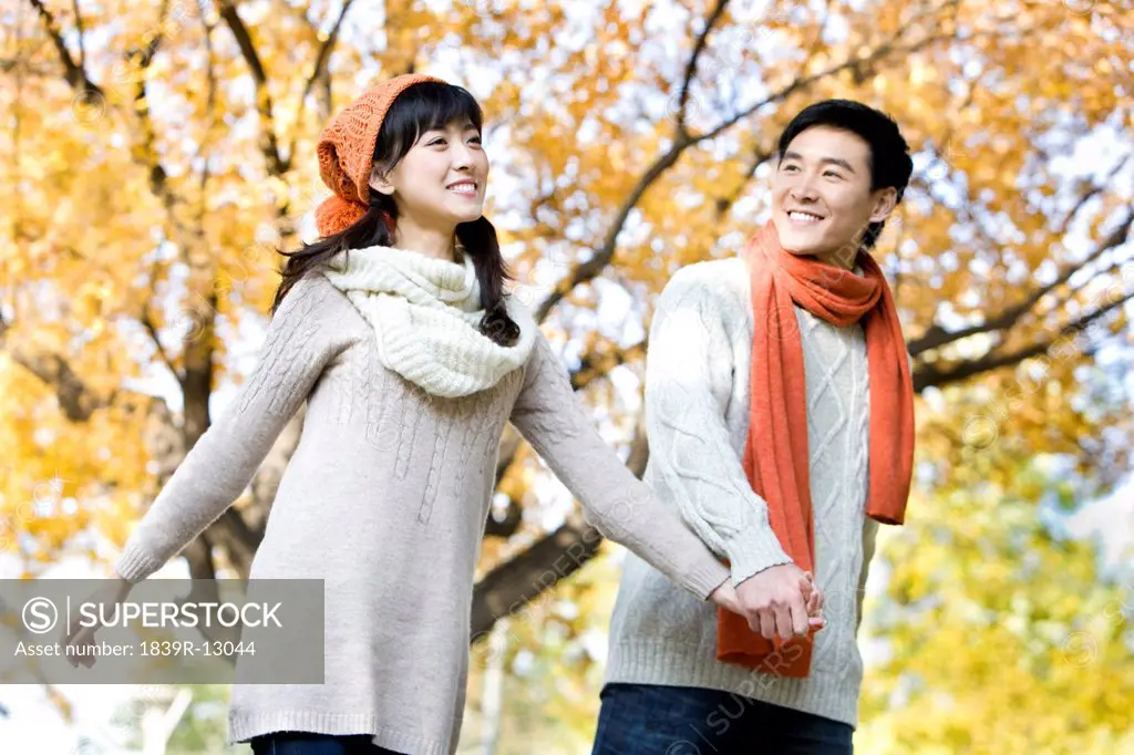 Young Couple Holding Hands, Strolling Through a Park
