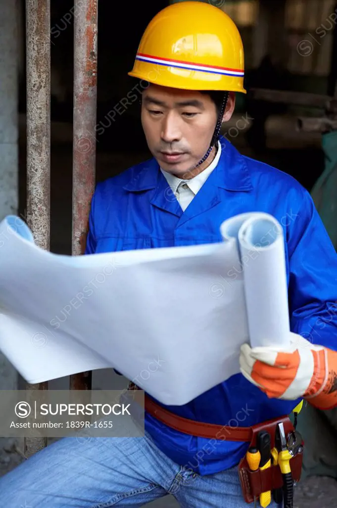 Man In Construction Site Wearing A Hard Hat And Holding Blueprints