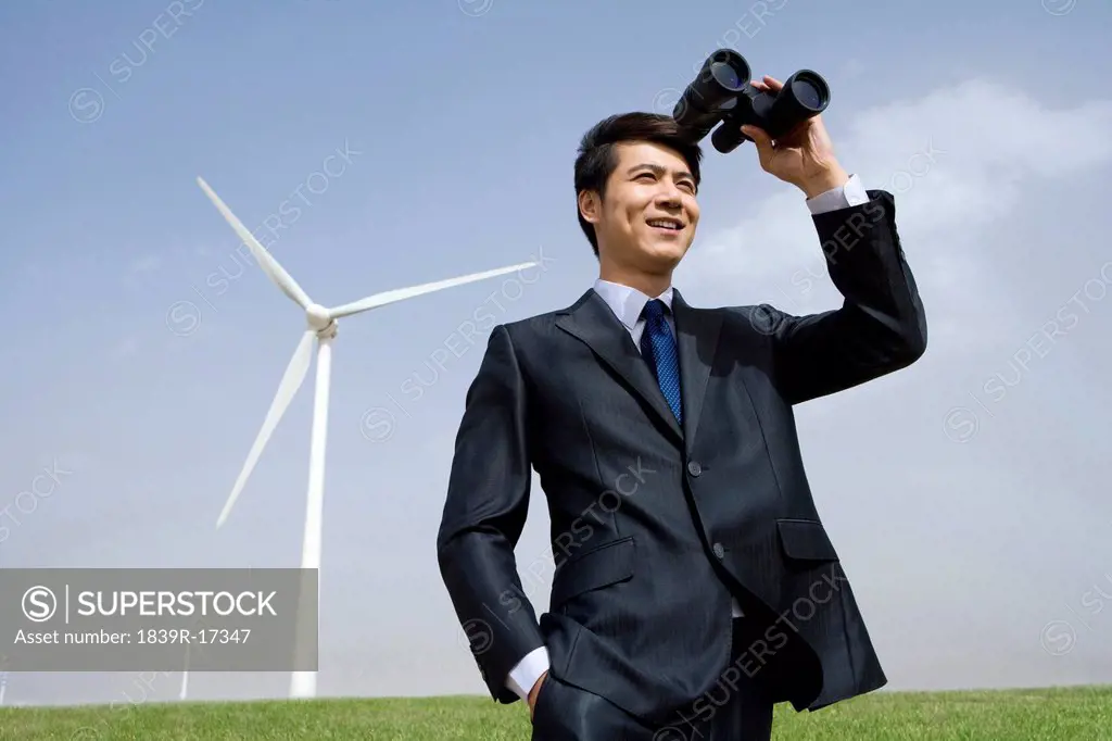 Portrait of a businessman using binoculars in front of wind turbine