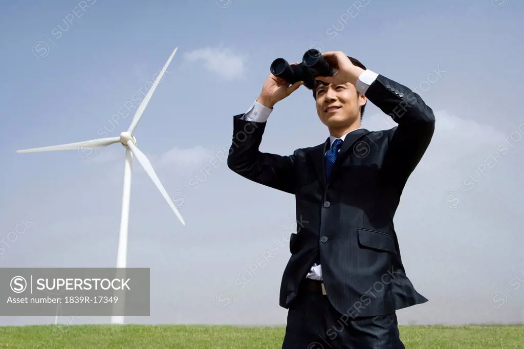 Portrait of a businessman using binoculars in front of wind turbine
