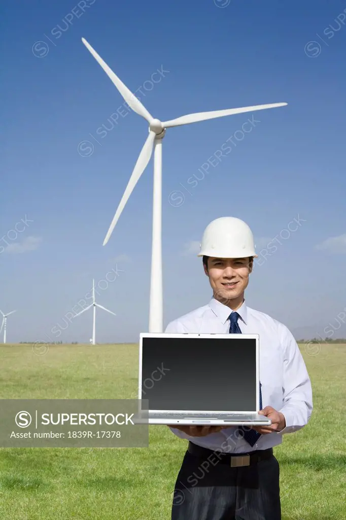 Engineer holding a laptop in front of wind turbines