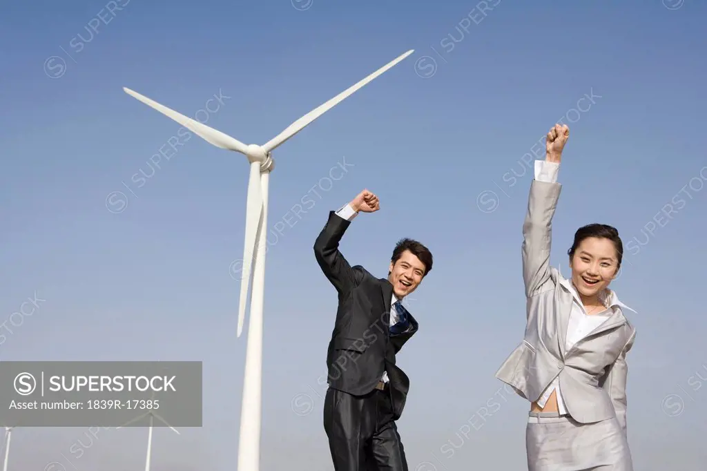 Businesspeople cheering in front of wind turbines