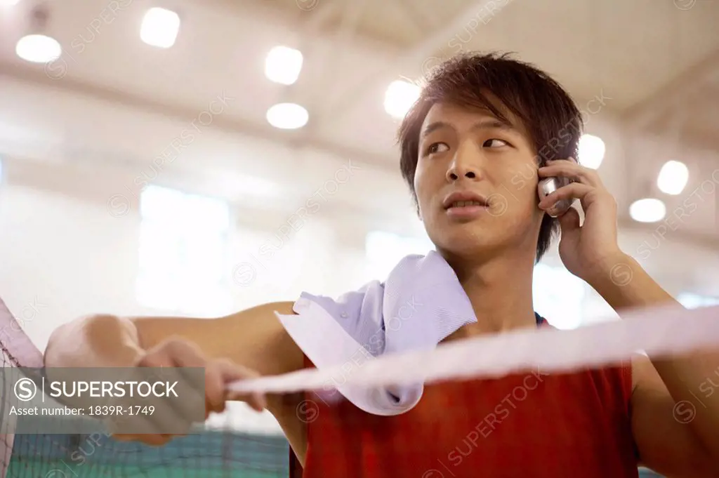 Man Leaning On Badminton Net Talking On Cellphone