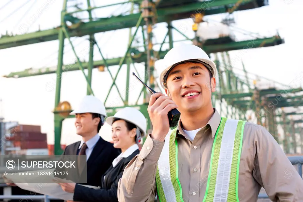 shipping industry worker using a walkie_talkie with businesspeople looking over blueprints in the background