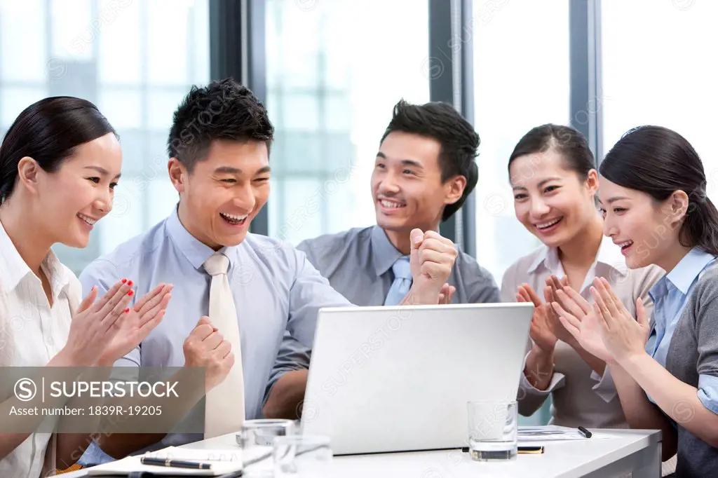 Businesspeople cheering while looking over a laptop