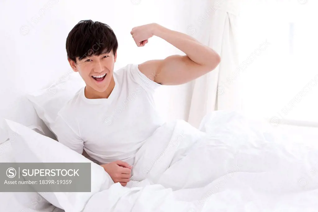 Young man showing strength in bed