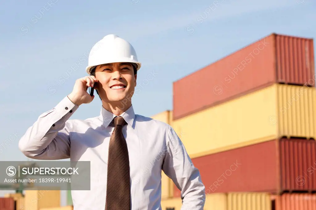 businessman on his cellphone with cargo containers in the background