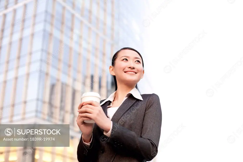A businesswoman with a cup of coffee outside office buildings contemplating