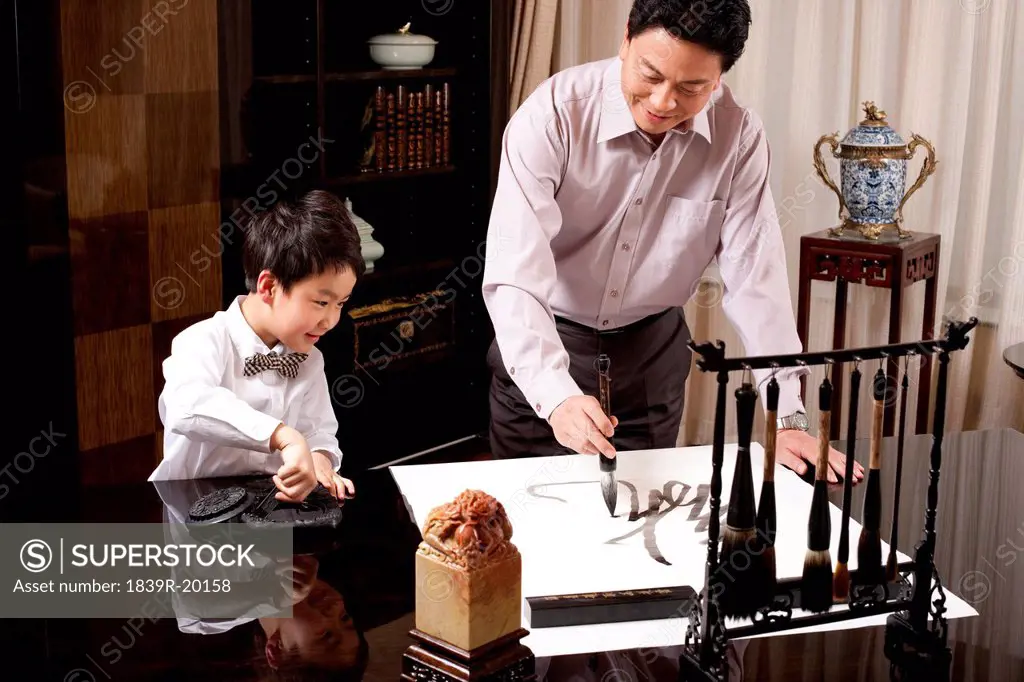 Grandpa and grandson practising Chinese calligraphy