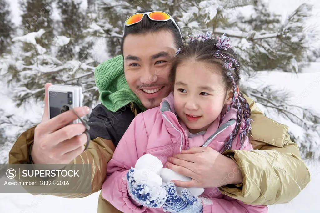 Father And Daughter Taking A Photo Of Themselves On Ski Field