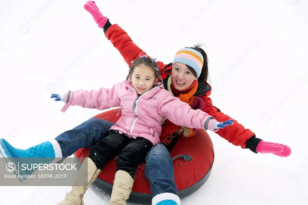 Mother And Daughter Riding On Inflatable Snow Tube
