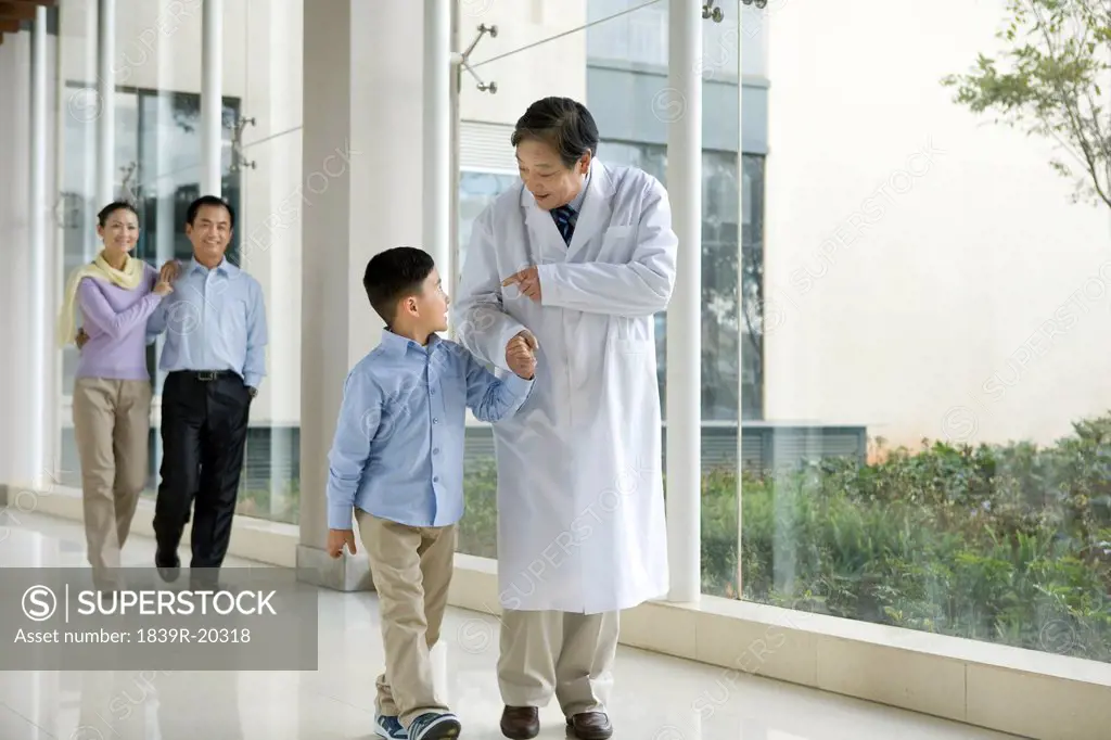 Young Family Walks in a Hospital Corridor With a Doctor