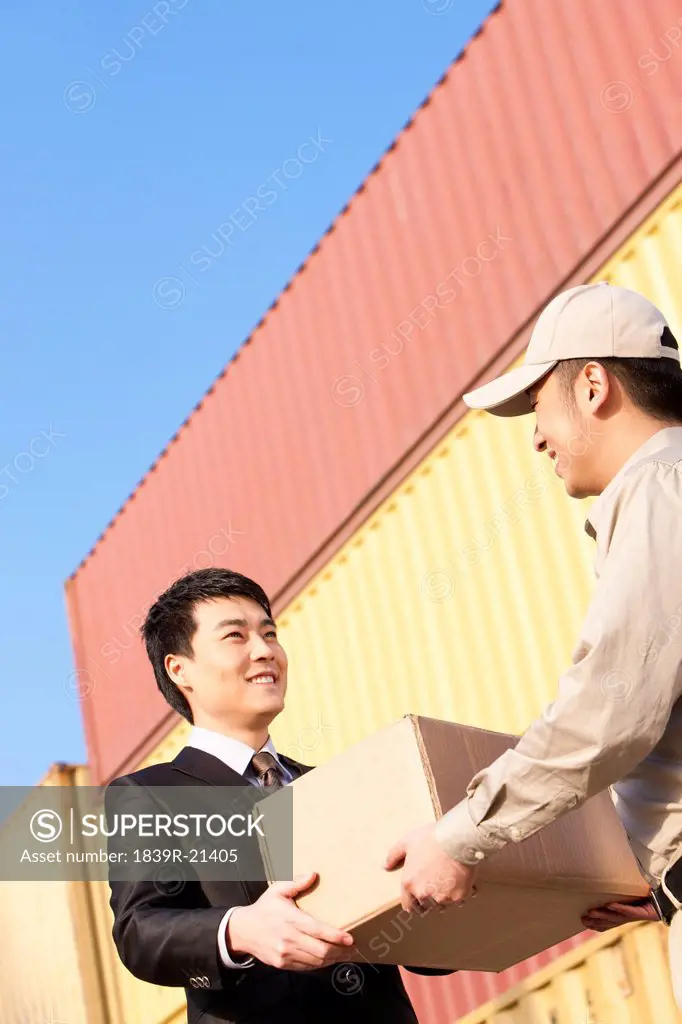 businessman and shipping industry worker giving and receiving a cardboard box