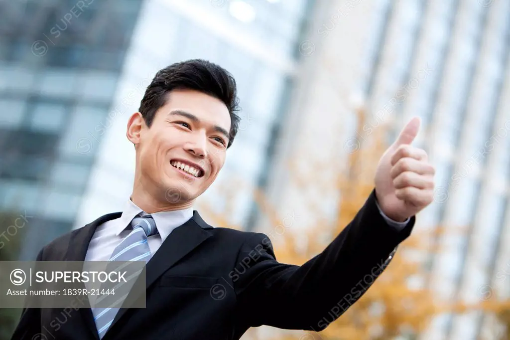 A businessman outside office buildings giving the thumbs_up