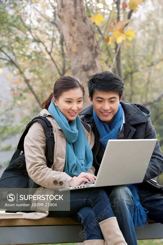 A young man and woman using a laptop together on a park bench