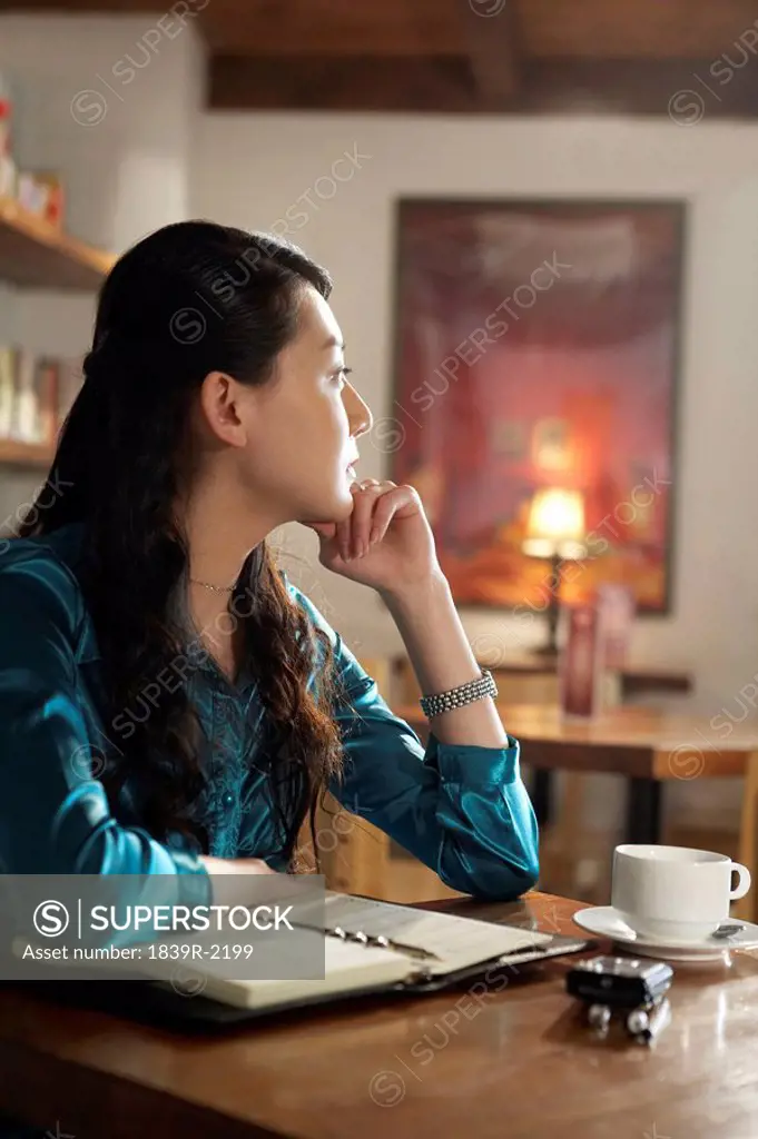 Woman Sitting At A Table With A Book Looking Contemplative