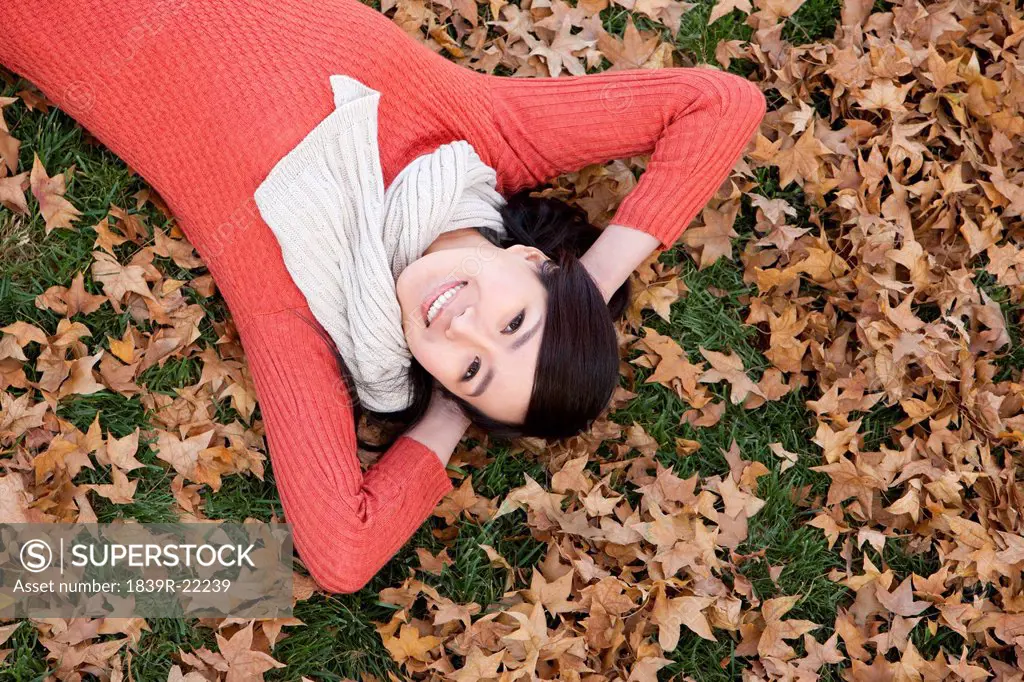 Young woman lying on the grass surrounded by Autumn leaves
