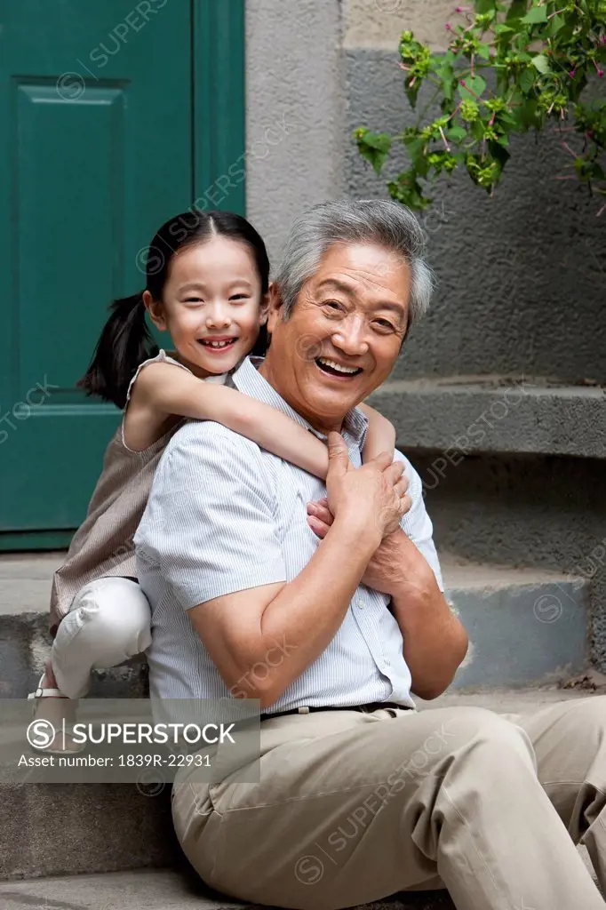 Chinese Grandfather and Grandaughter embracing on front stoop