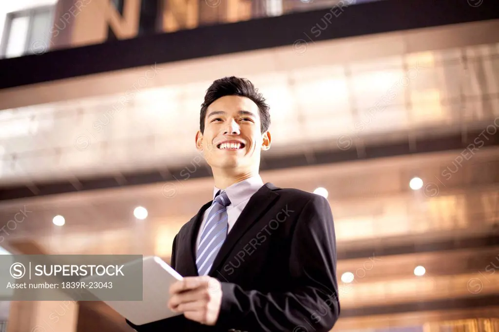 A businessman using a digital tablet outside an office building at night