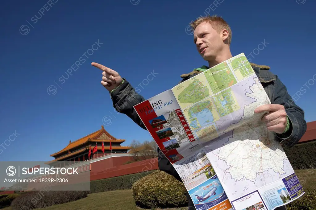 Young Man Using Map And Pointing In The Right Direction