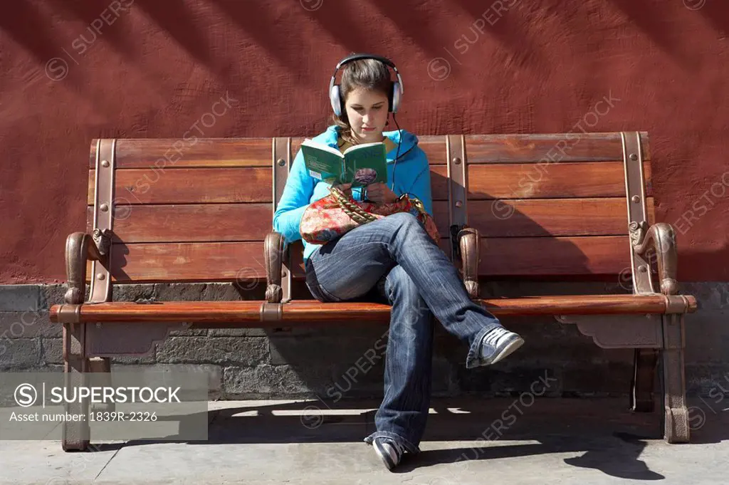 Young Woman Reading And Listening To Headphones