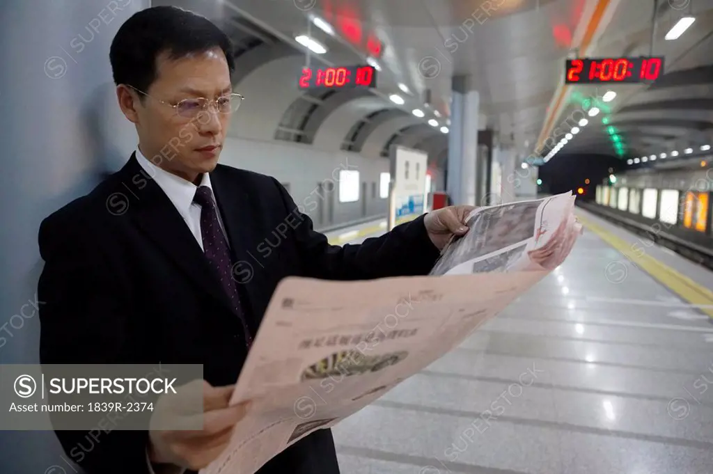 Businessman Reading Newspaper In Train Station