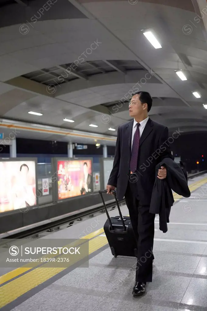 Businessman Pulling Suitcase Along In Train Station