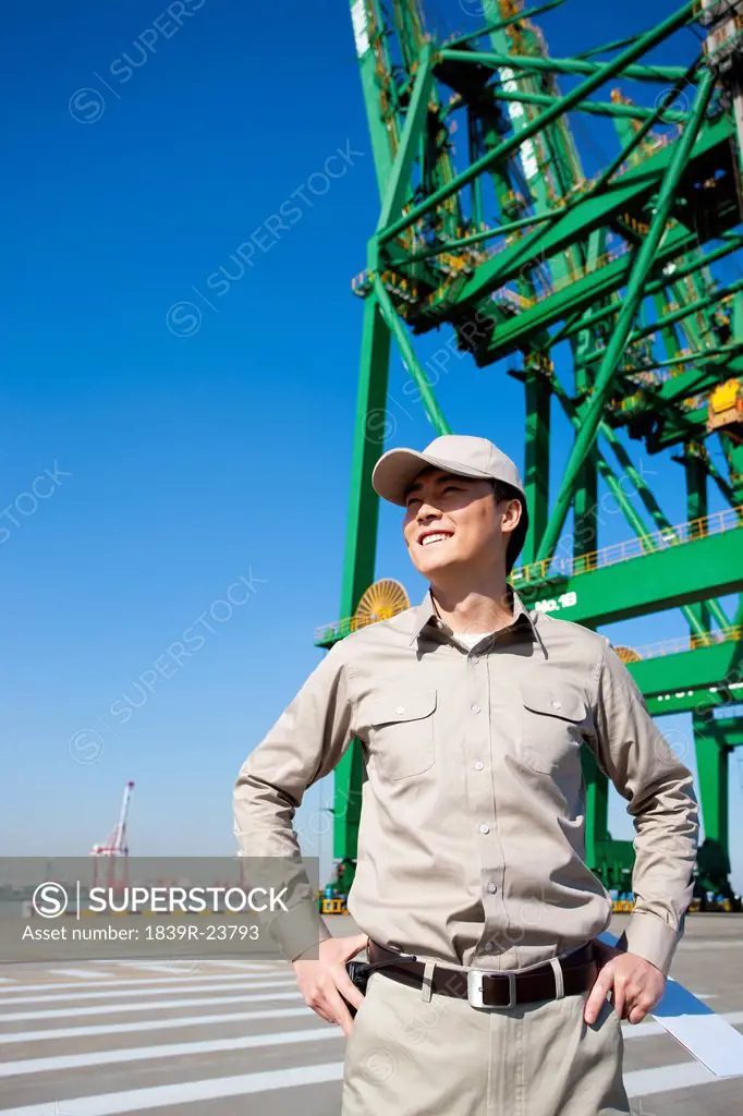 Male shipping industry worker with hands on hips with shipping dock background