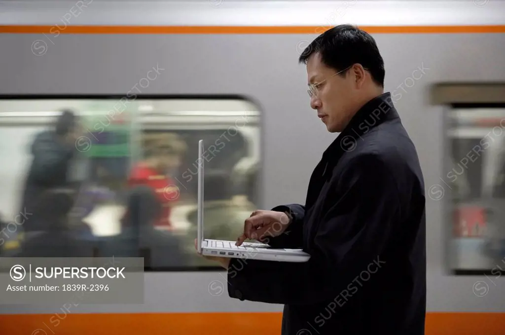A Man Uses His Laptop As The Subway Train Passes By In The Background