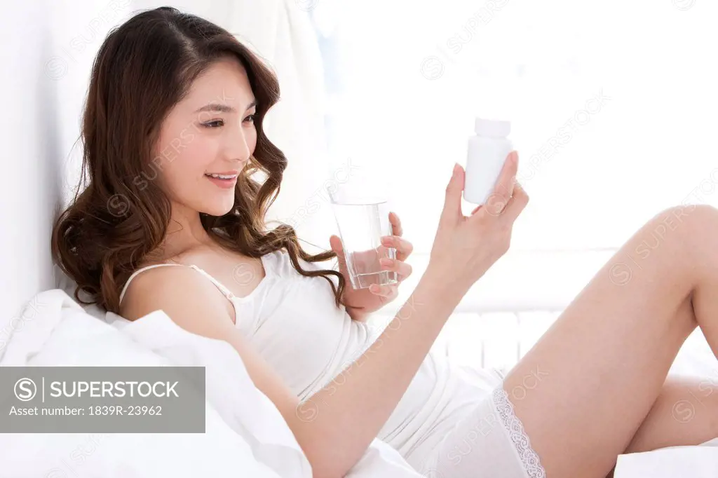 Young woman taking medicine in bed