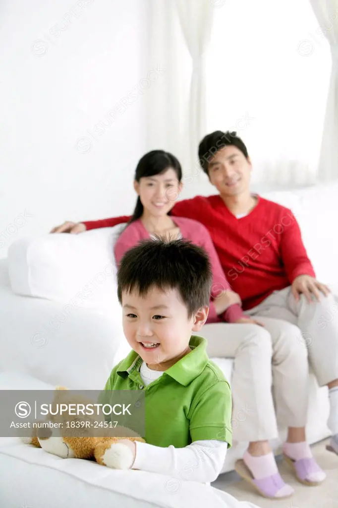 Young Chinese boy with teddy bear and parents in the background