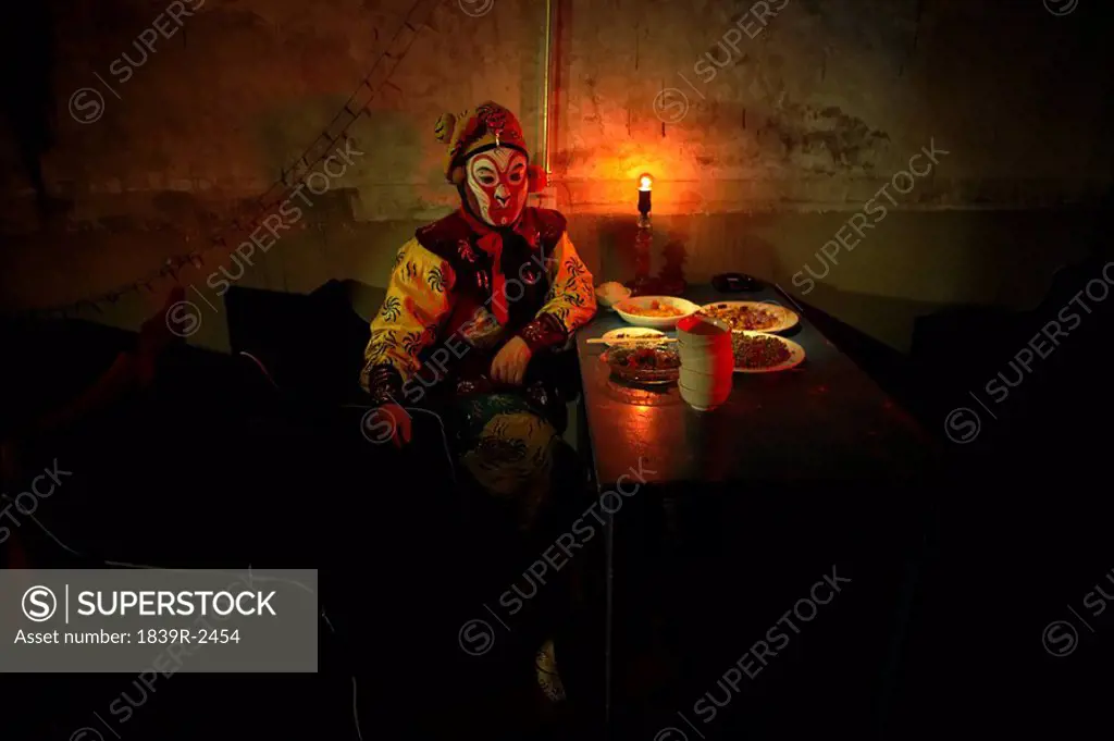 Man In Ceremonial Costume Sitting At Table With Food