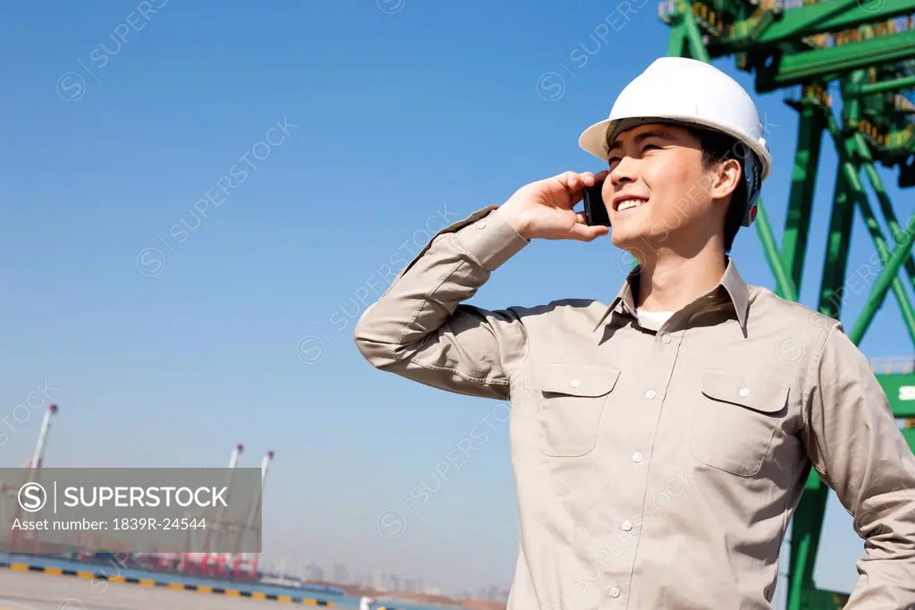 Male shipping industry worker on the phone with shipping dock background