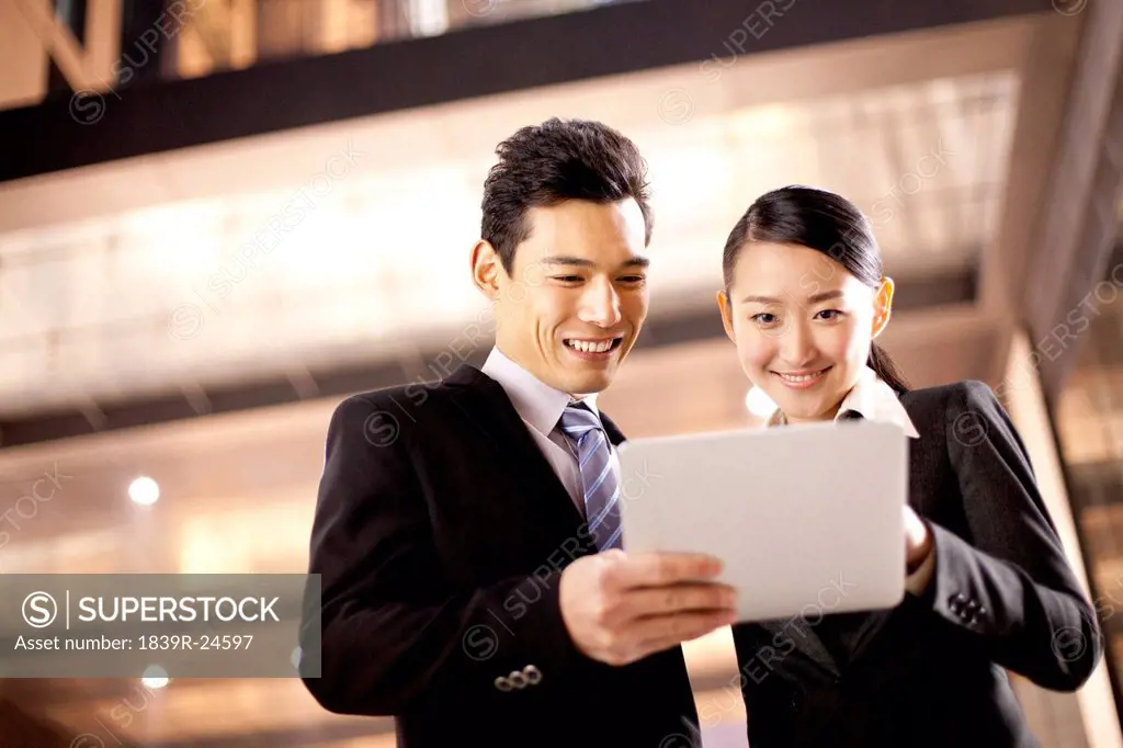 A businessman and businesswoman using a digital tablet outside an office building at night