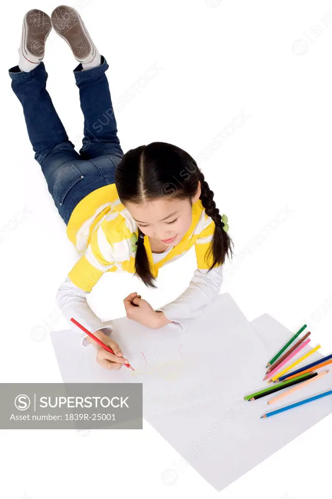 A young girl coloring while lying on the floor