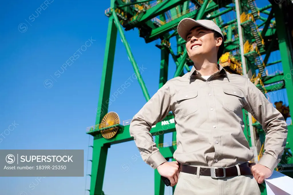 Male shipping industry worker with hands on hips with shipping dock background
