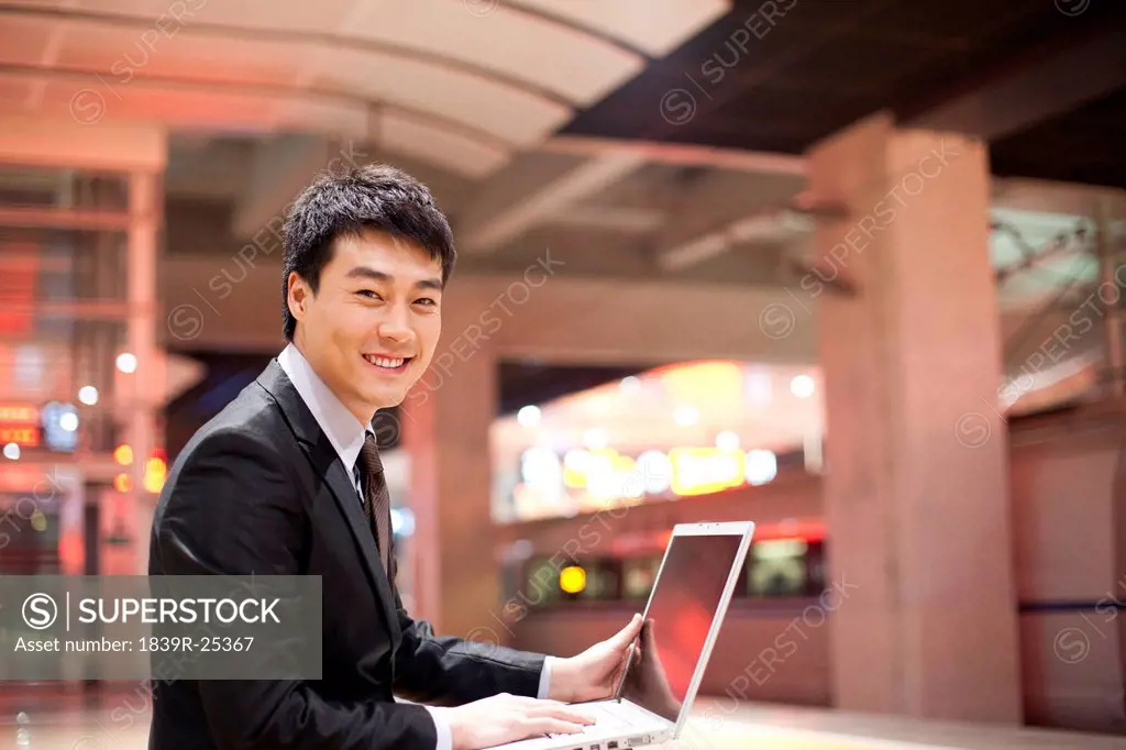 Young businessman using his laptop at the train station