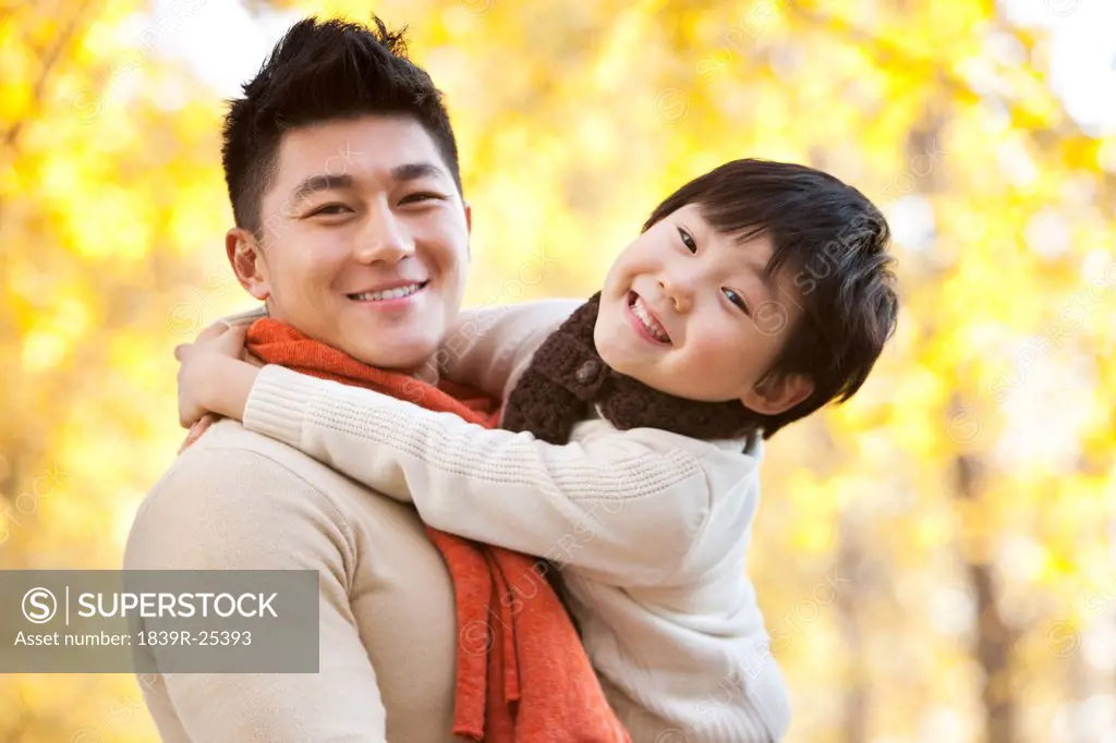 Father carrying son surrounded by Autumn trees in the background