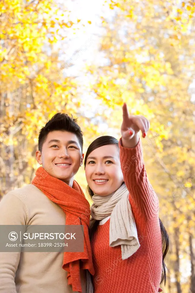 Young couple standing and pointing with Autumn leaves in the background