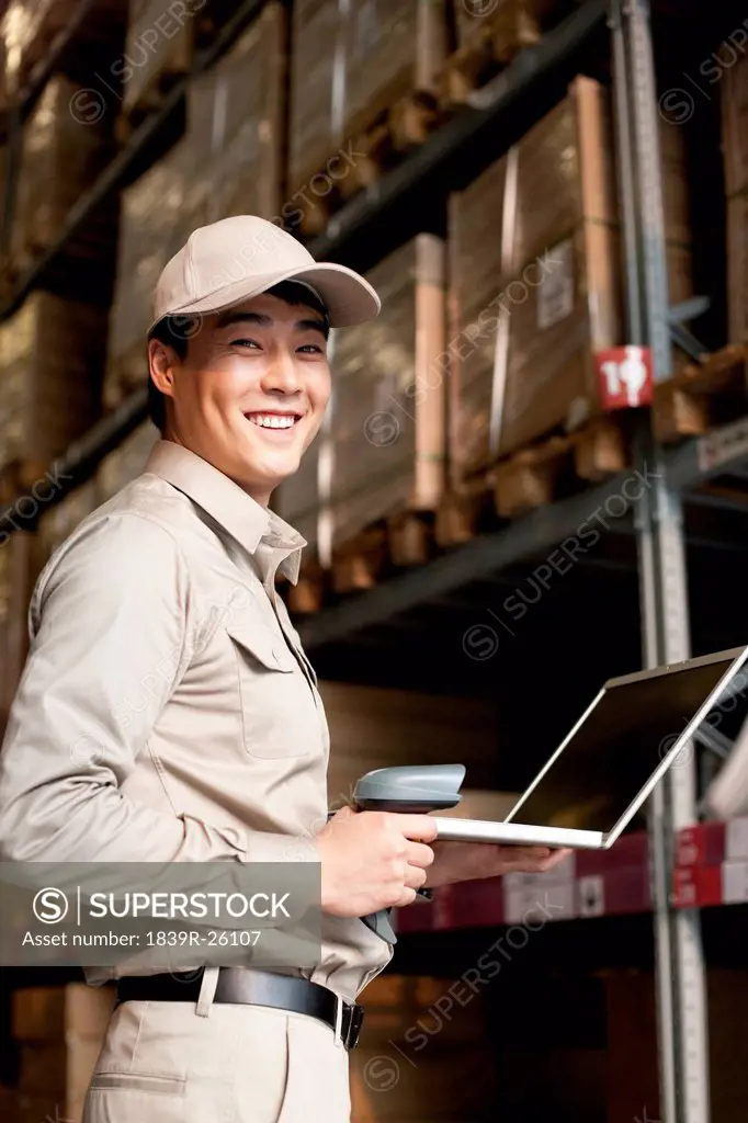 Male Chinese warehouse worker with laptop and scanner